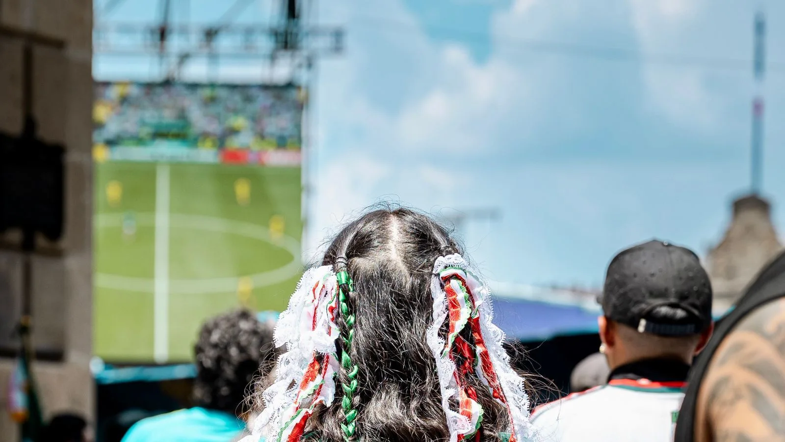 A Mexico fan with green-white-red ribbons in her hair watches the match on a big screen at a Mexico City fan fest — hosts Mexico beat Czechia 3-0 to win World Cup 2026 Group A with a perfect record